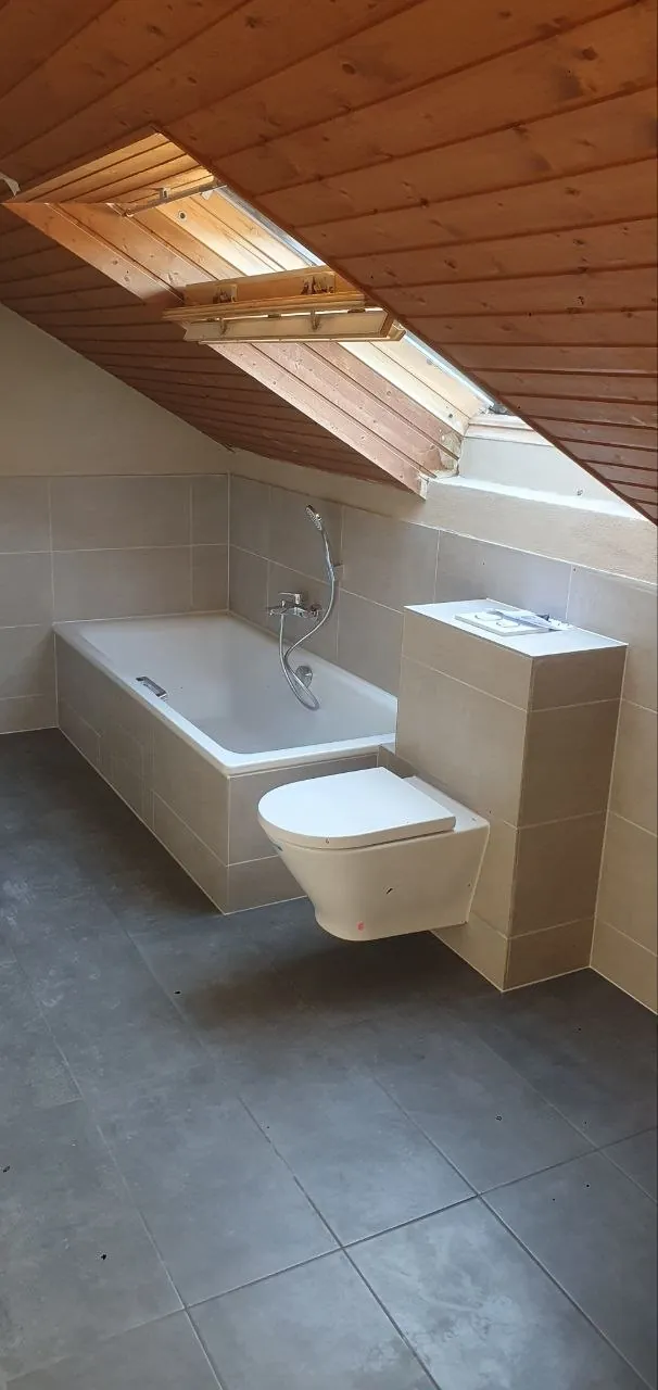 Badewanne und Wand-WC unter der Dachschräge, grau gefliest