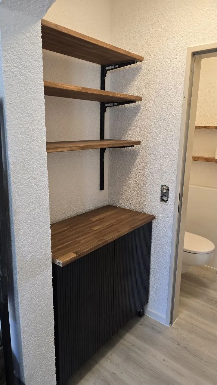 Möbel nach Maß für eine Wandnische: Regalböden aus Holz über einem schwarzen Unterschrank
